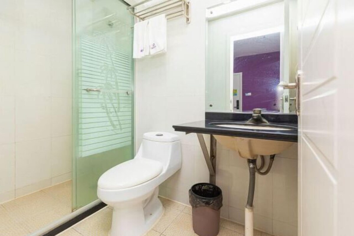 A bathroom with a toilet, a glass shower enclosure, a sink with a mirror, and a trash bin.