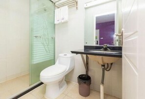 A bathroom with a toilet, a glass shower enclosure, a sink with a mirror, and a trash bin. - Colorful Art Hotel Shanghai (Shanghai)