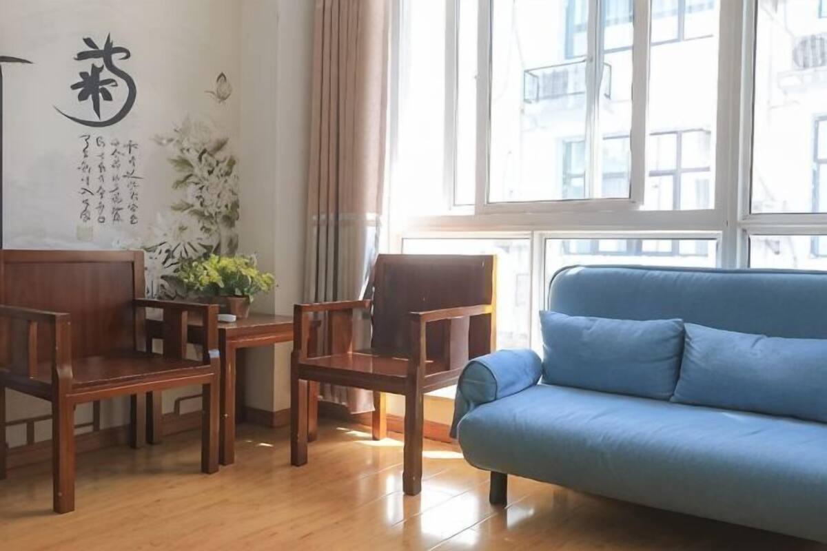 A room with a blue sofa, wooden chairs, a small table with a plant, and a window with a view of buildings.