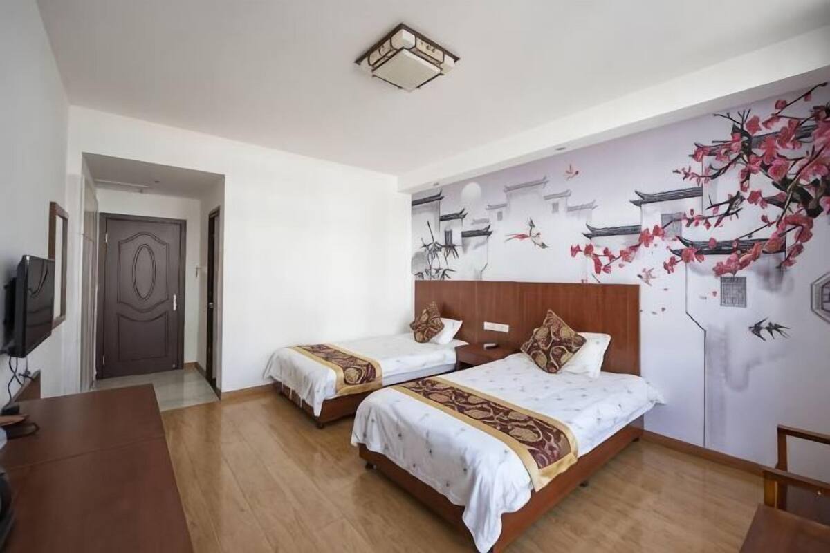 A hotel room with two beds, a wooden desk, a television, and a mural on the wall.