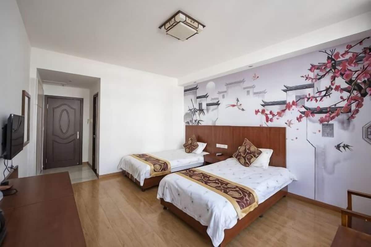 Une chambre dâhĂŽtel avec deux lits, un bureau en bois, une tĂ©lĂ©vision et une fresque murale.