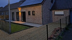 A modern brick house with a sloped roof, solar panels, and a well-lit entrance.