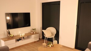 A modern living room with a flat-screen TV, a wooden coffee table, a white chair, and a sofa.