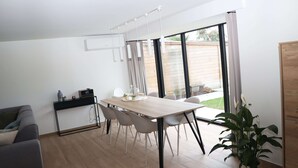 A modern living room with a dining table, grey sofa, and a potted plant.