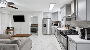 A compact kitchen with white cabinets, a stainless steel refrigerator, a stove, and a microwave.