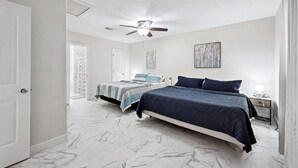 A bedroom with two beds, a ceiling fan, and artwork on the walls.