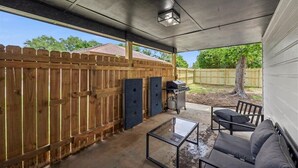 A covered patio area with a wooden fence, a grill, and outdoor seating.
