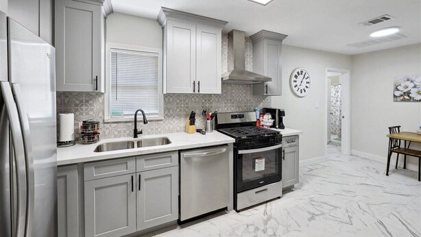 A modern kitchen with white cabinets, a stainless steel refrigerator, a stove, and a dishwasher.