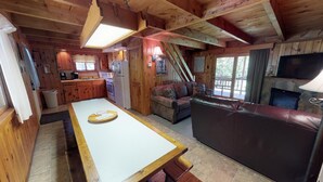 Een blokhut interieur met een keuken, eethoek en woonkamer, met houten wanden en een stenen openhaard.