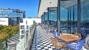 A rooftop terrace with checkered flooring, glass railings, and outdoor seating.