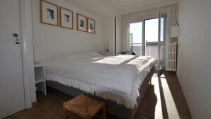A bedroom with a bed, a chair, a window, and a door. - Apartment in Belgium Near Seafront & Casino (Knokke-Heist)