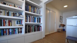A room with white built-in bookshelves filled with books, a wooden floor, a small wooden bench, and a radiator. - Apartment in Belgium Near Seafront & Casino (Knokke-Heist)