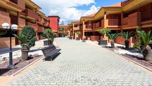 A courtyard with a paved walkway, benches, potted plants, and a building with balconies.