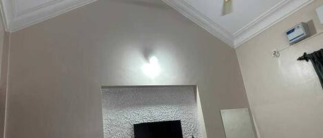 Una habitación con ventilador de techo, televisor montado y un espejo en la pared.