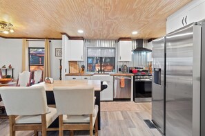 A modern kitchen with a wooden ceiling, stainless steel appliances, and a dining area with white chairs. - Tranquil dog-friendly 3-bedroom house in Pinetop with fenced-in backyard (Pinetop-Lakeside)