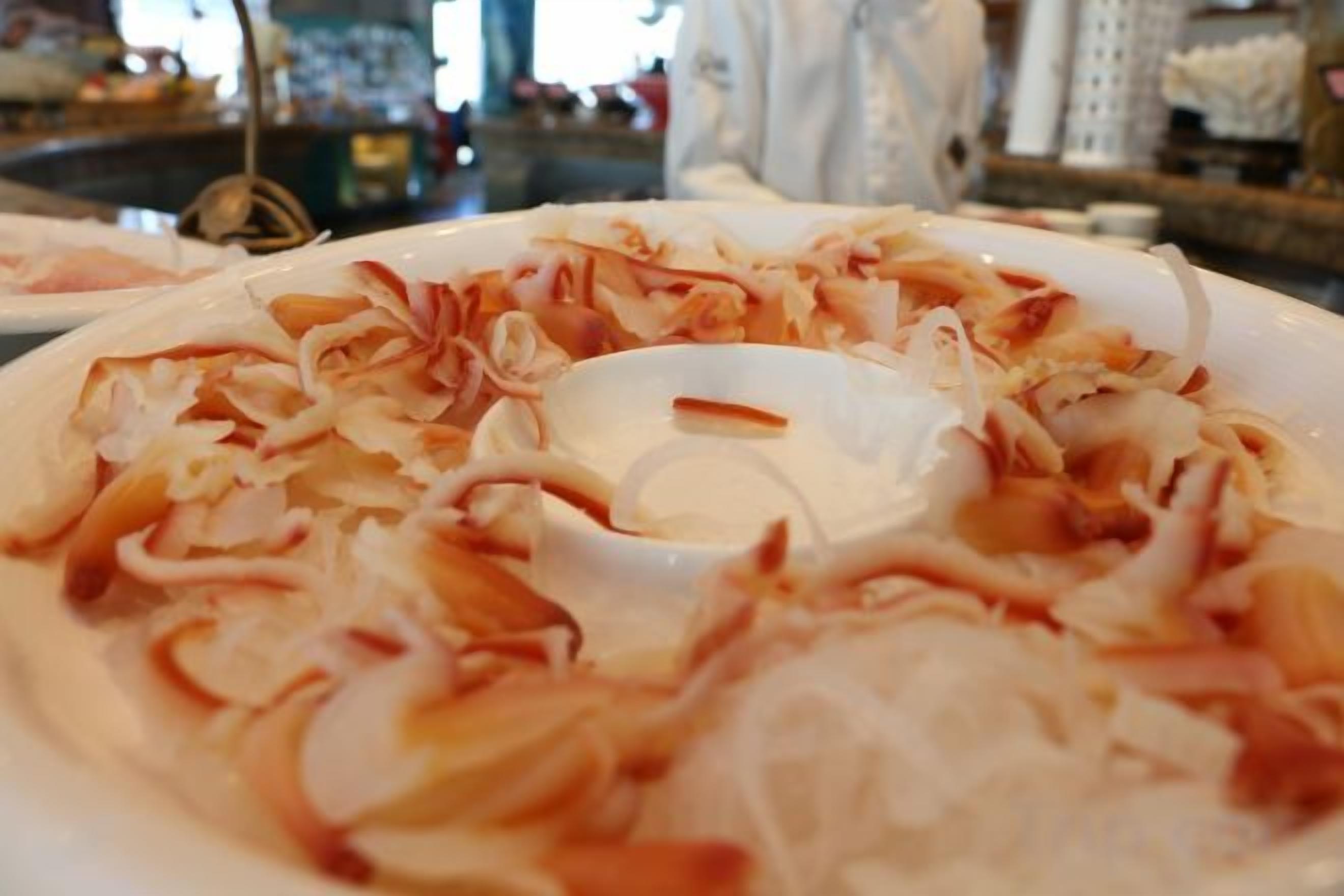 Une assiette contenant des aliments coupés en fines lanières, peut-être une salade ou une entrée, avec un bol blanc au centre.
