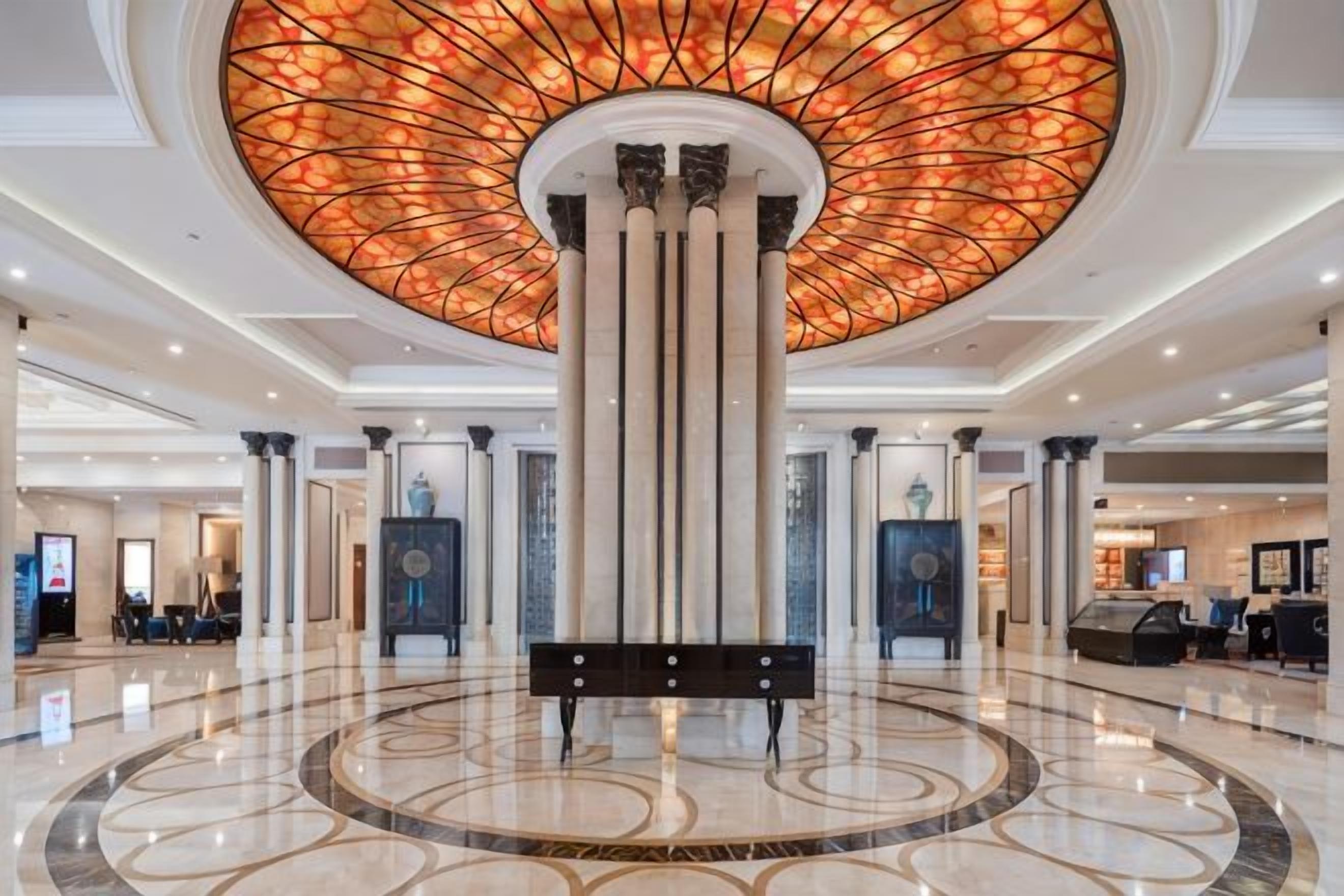 Een hotel lobby met een rond vloerontwerp, een centrale kolom en een plafond met een cirkelvormig glas-in-lood patroon.