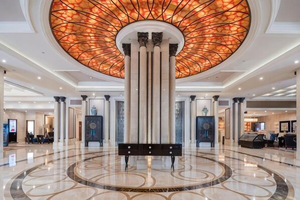 A hotel lobby with a circular floor design, a central column, and a ceiling with a circular stained glass pattern. - Ramada Plaza by Wyndham Tian Lu Hotel Wuhan (Wuhan)