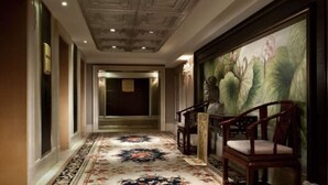 A hallway with a patterned carpet, wooden chairs, and a large floral painting on the wall. - Ramada Plaza by Wyndham Tian Lu Hotel Wuhan (Wuhan)