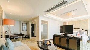 A hotel room with a sofa, a TV on a cabinet, a desk, and a bed. - Ramada Plaza by Wyndham Tian Lu Hotel Wuhan (Wuhan)