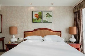 A hotel room with a large bed, two bedside tables with lamps, a wooden headboard, and two framed floral paintings on the wall. - Ramada Plaza by Wyndham Tian Lu Hotel Wuhan (Wuhan)