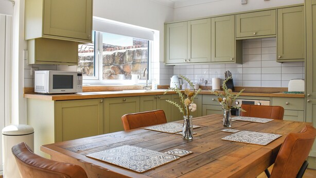 Una cocina con armarios verdes, una mesa de comedor de madera y una ventana con vistas.