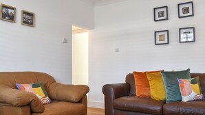 Una sala de estar con dos sofás de cuero marrón, cojines coloridos, una mesa de centro de madera con un objeto decorativo y cuadros enmarcados en la pared.
