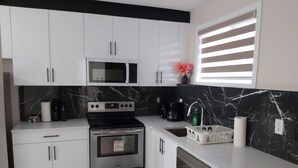 A modern kitchen with white cabinets, a black and white marble backsplash, stainless steel appliances, and a window with blinds. - Luxurious 2 BDRMS Basement Legal Suite (Edmonton)