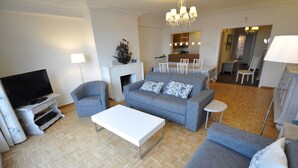 A modern living room with a grey sofa, white coffee table, and a flat-screen TV. - Apartment in Duinbergen Near Sandy Beach (Knokke-Heist)