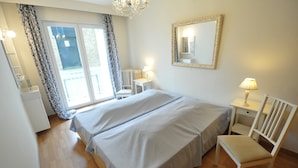 A bedroom with a double bed, a chair, a desk, a mirror, and a window with curtains. - Apartment in Duinbergen Near Sandy Beach (Knokke-Heist)