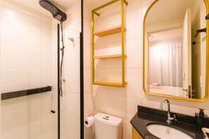 Et badeværelse med bruser, toilet, vask og et spejl med gylden ramme.