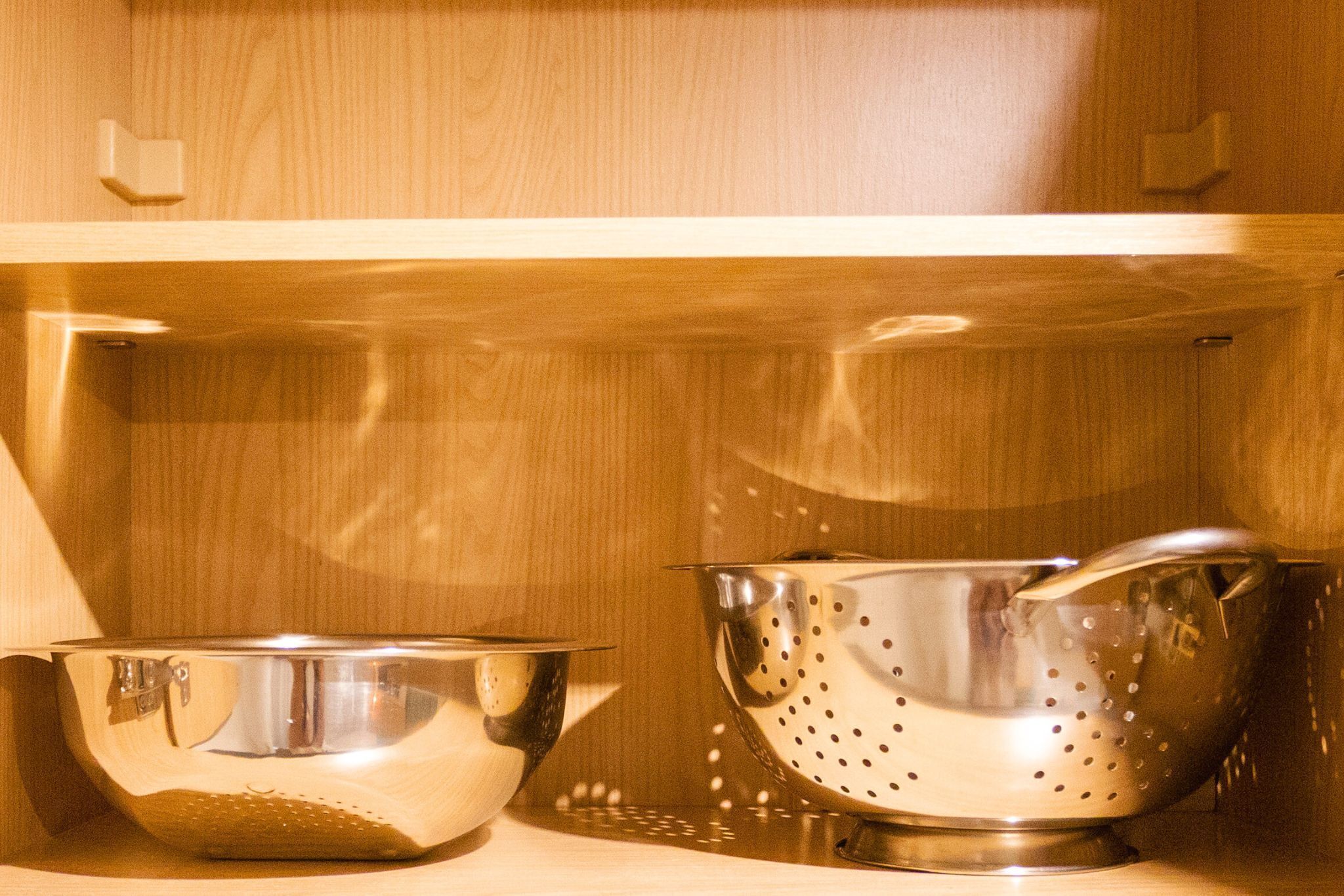 A kitchen shelf with a stainless steel colander and a stainless steel bowl.