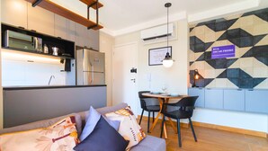 Una cocina moderna con electrodomésticos integrados, un comedor con mesa y sillas, y una sala de estar con sofá y cojines.
