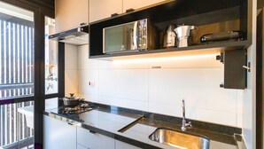 Una cocina moderna con estufa a gas, lavamanos de acero inoxidable y microondas sobre un estante negro.