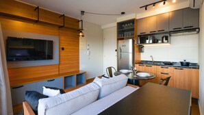 Un espacio habitable compacto con sofá, una mesa de comedor, y una zona de cocina equipada con refrigerador, microondas y armarios.