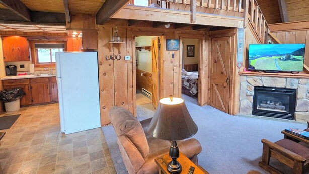 Un intérieur rustique avec une chambre en mezzanine, une cheminée, un téléviseur et un coin cuisine.