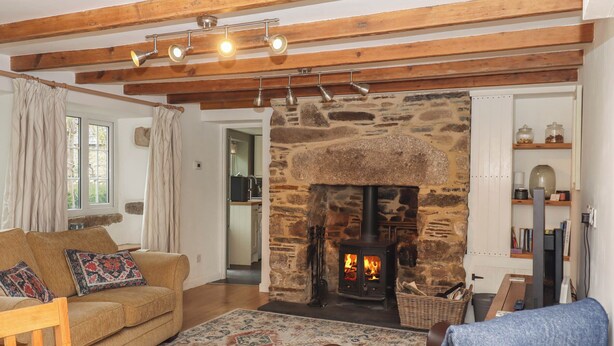 Una sala de estar acogedora con chimenea de piedra, vigas de madera, un sofá y una mesa de comedor con cosas para el desayuno.