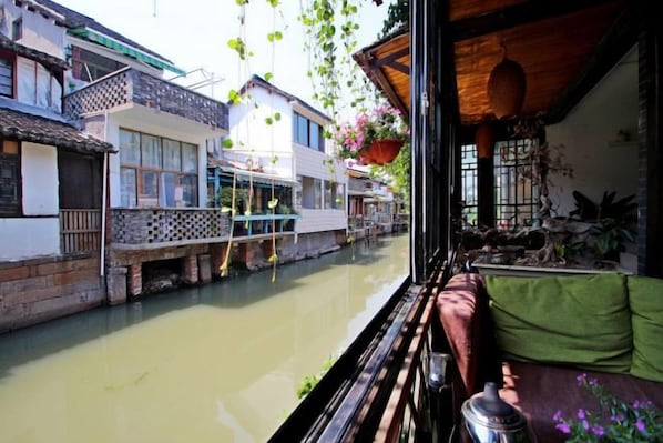 A traditional building with a balcony overlooking a canal, with hanging plants and a view of the water.