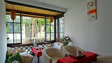 Una habitación con vistas a zonas verdes, muebles de mimbre y un mantel rojo.