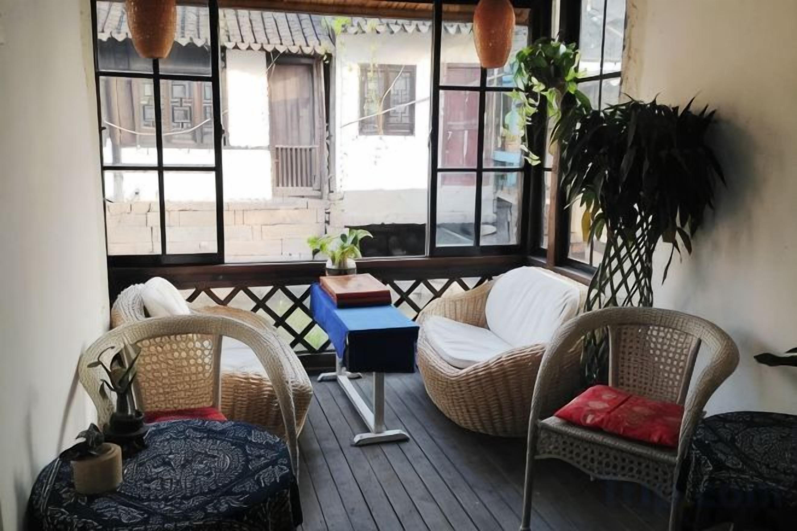 Un espacio de estar al aire libre techado, con muebles de mimbre, una mesa pequeña y una planta en maceta.