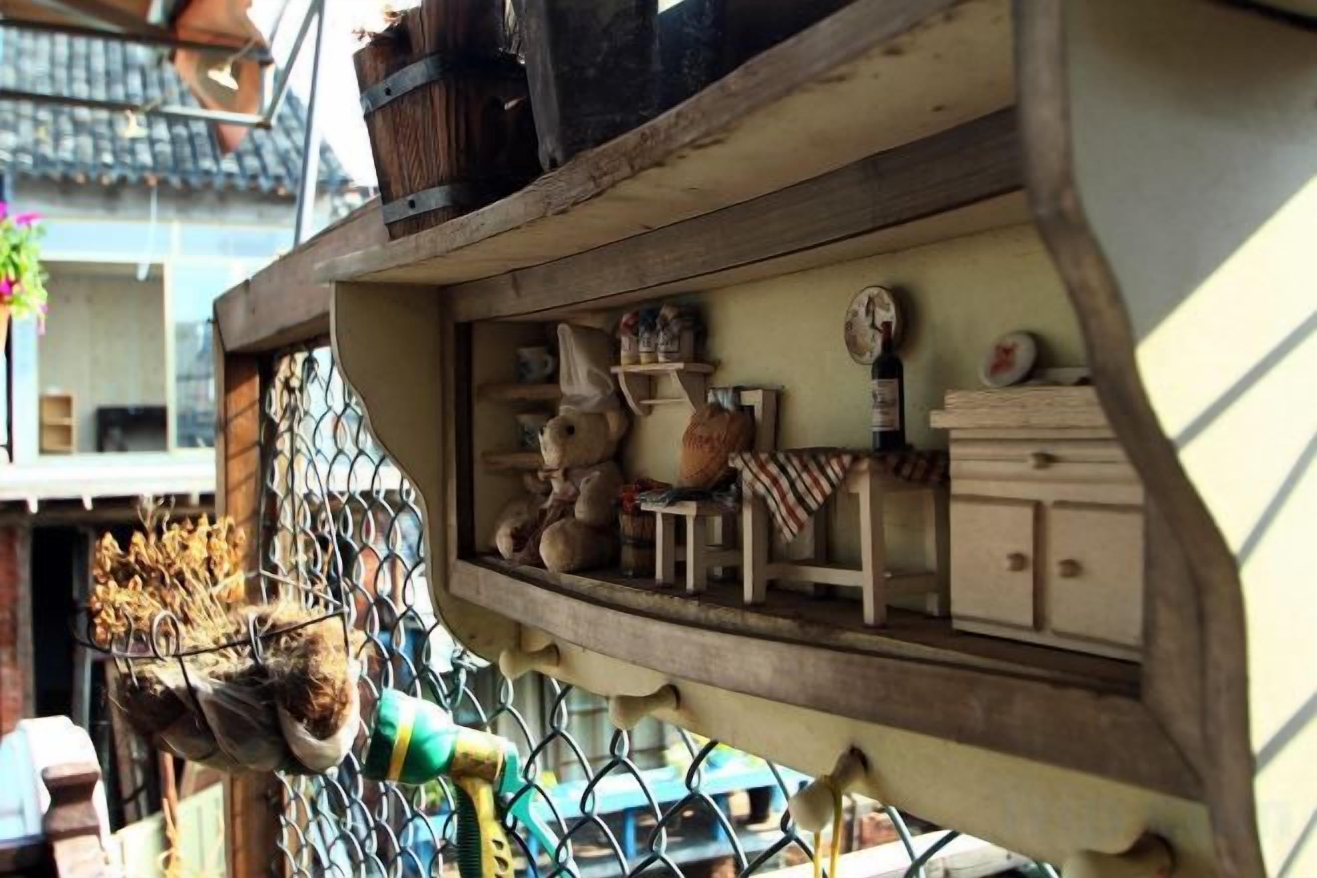 A small, enclosed space with a wooden shelf containing various items like a clock, a vase, and a small table.