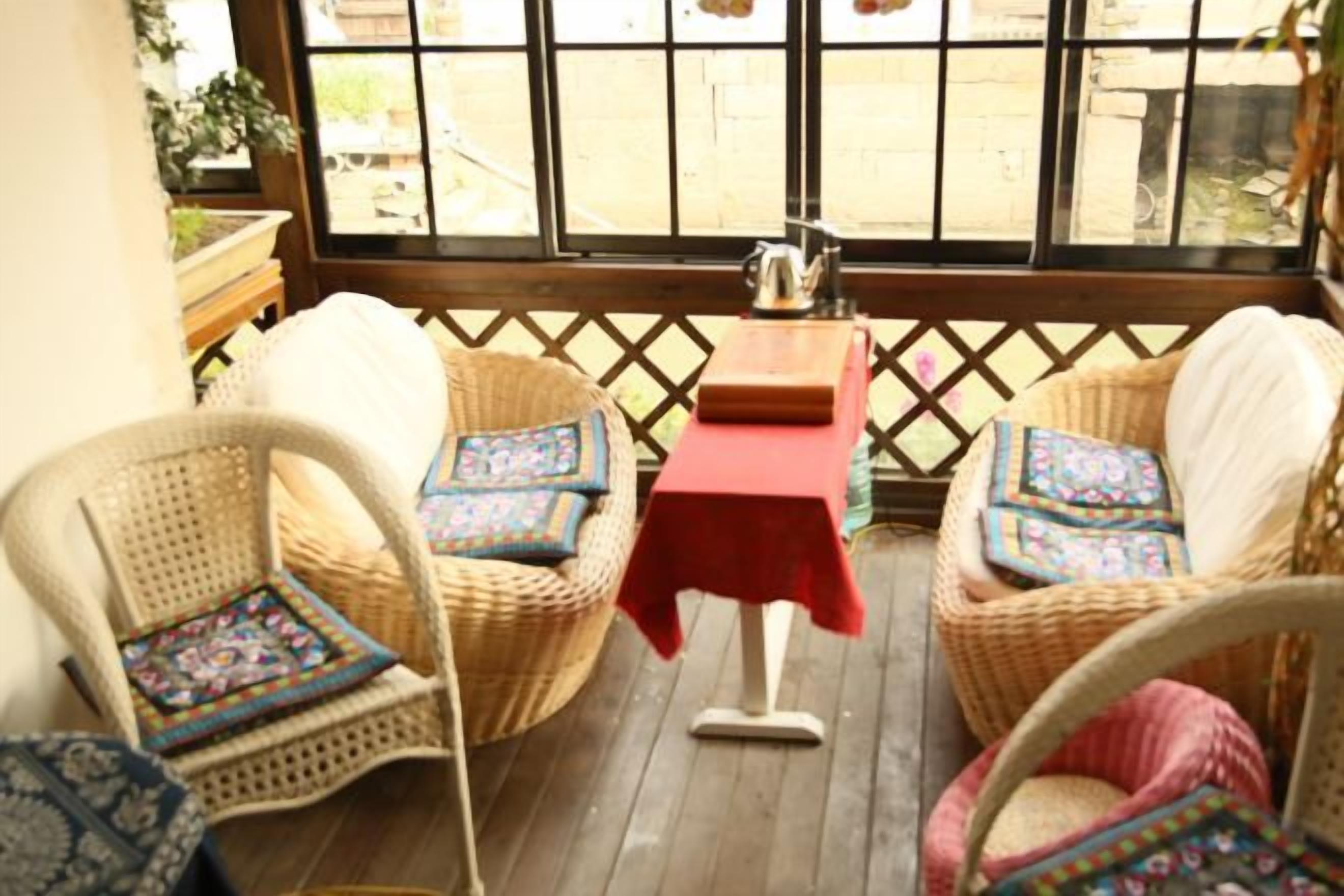 Una silla de mimbre con cojín y una mesita con mantel rojo.