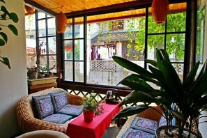 A room with a wicker sofa set, a red table, and a view of a traditional building through large windows. - Shanghai Jiaoli Xiaoyan Inn (Zhujiajiao Scenic Area Ancient Town) (Shanghai)