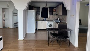 A modern kitchen with a central island, a washing machine, and a dining area with black wire chairs.