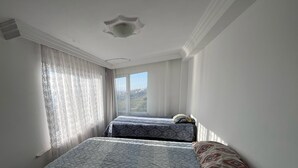 A room with two beds, a window with curtains, and a plain ceiling.