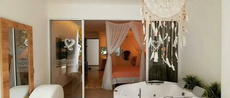 A modern bedroom with a large bed, a vanity with a mirror, and a dreamcatcher hanging from the ceiling.