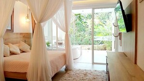 Un dormitorio con cama con dosel, un televisor de pantalla plana montado en la pared y vistas a un jardín exuberante a través de amplias puertas correderas de vidrio.