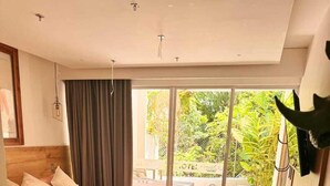 Habitación de hotel moderna con cama de madera, un escritorio pequeño y vista a un jardín a través de una puerta corrediza de vidrio.