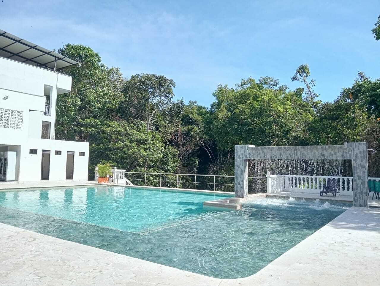 A swimming pool with a waterfall feature, surrounded by lush greenery and a modern building.