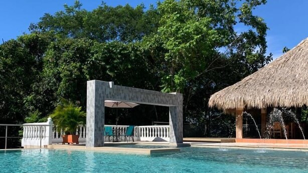 Una piscina cristalina con una estructura de techo de paja y una zona de estar techada.